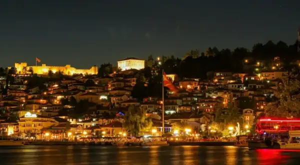 Oświetlone miasto nad jeziorem nocą, z twierdzą na wzgórzu. Czy warto wybrać się na wakacje w Macedonii? Zdecydowanie tak!