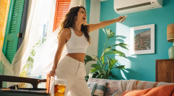 Femme joyeuse ajustant le **dehum climatiseur** avec une télécommande, profitant de la fraîcheur dans un salon lumineux.