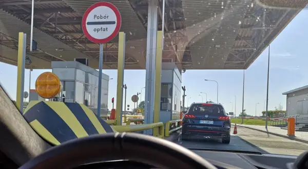 Kolejka samochodów na autostradzie A4 przed punktem poboru opłat. Widać bramki, znaki drogowe i samochody czekające na przejazd.