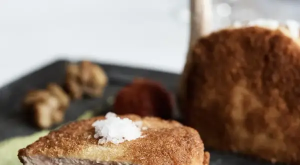 Ein knuspriges Kalbsschnitzel, italienisch zubereitet, mit feinen Beilagen auf einem dunklen Teller.