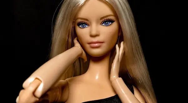 Lalka Barbie z blond włosami i niebieskimi oczami, w czarnej sukience, symbolizuje emancypację kobiet.