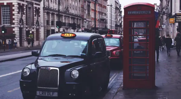 Czarne taksówki i czerwona budka telefoniczna na ulicy w Londynie.