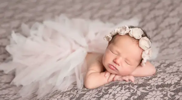 Un bébé endormi, paré d'une couronne de fleurs et d'une jupe en tulle, évoque la douceur et la pureté. Sa pose paisible invite à réfléchir à la signification prénom.