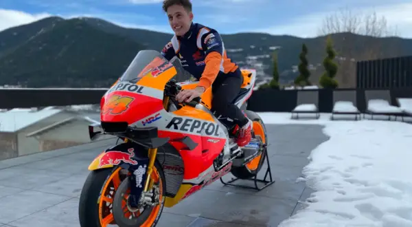 Piloto de Honda MotoGP con su moto Repsol, listo para la temporada, con montañas nevadas de fondo.