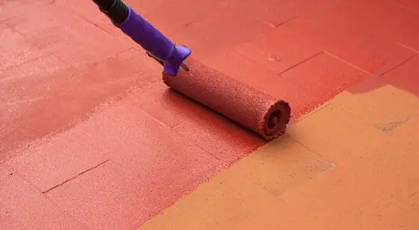 Rodillo aplicando pintura para suelos de exterior de color rojo sobre baldosas.