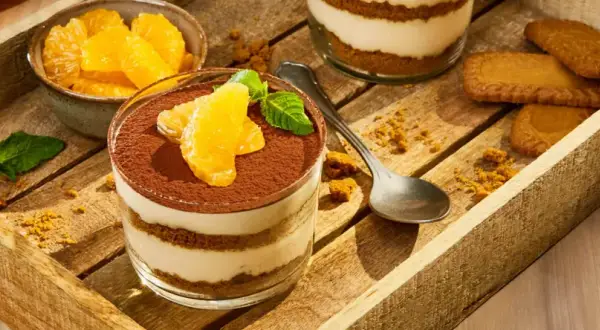 Délicieux tiramisu aux fruits d'orange, garni de cacao et de menthe fraîche, servi dans un verre sur un plateau en bois avec des biscuits.