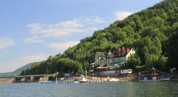 Malowniczy zbiornik wodny z zaporą, budynkami hotelowymi na zboczu góry i łodziami przy brzegu.
