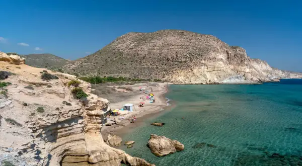 La cala del Peñón Blanco, con su arena dorada y aguas cristalinas, invita a disfrutar del sol bajo un cielo azul.