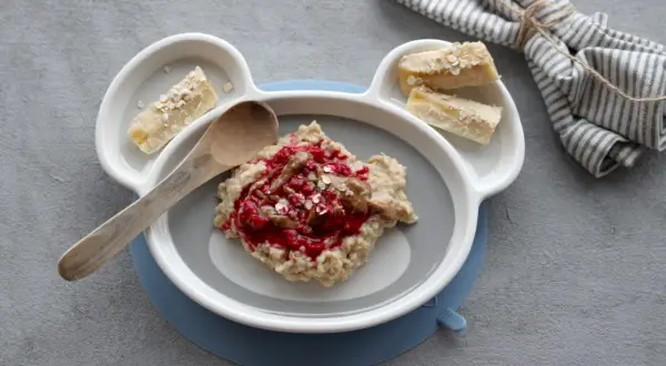 Leckerer Morgenbrei für Babys mit Beeren und Bananenstückchen auf einem Teller in Bärenform.