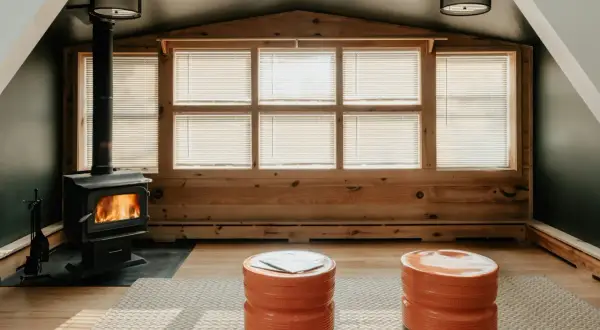Une cheminée dans une véranda confortable, avec des flammes vives réchauffant la pièce. Deux poufs orange vif invitent à la détente.