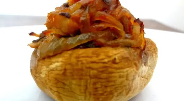 Gros plan sur un champignon farci, garni d'oignons caramélisés et d'herbes. Un délice à savourer !