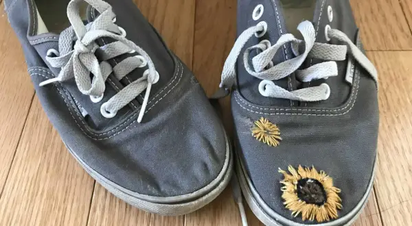 Paire de chaussures grises avec des lacets blancs. L'une des chaussures est ornée de broderies de tournesols, donnant un air bohème à ces chaussures trouées.