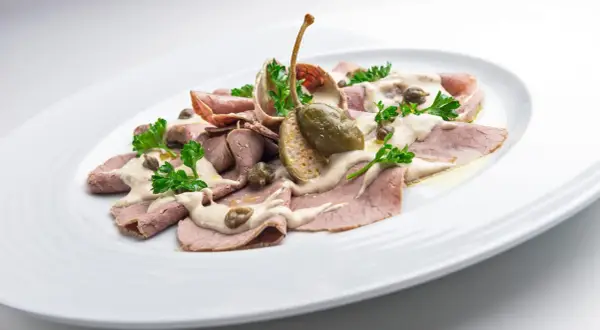 Vitello Tonnato: Dünne Kalbfleischscheiben mit Thunfischsauce, Kapern und Petersilie auf einem weißen Teller.