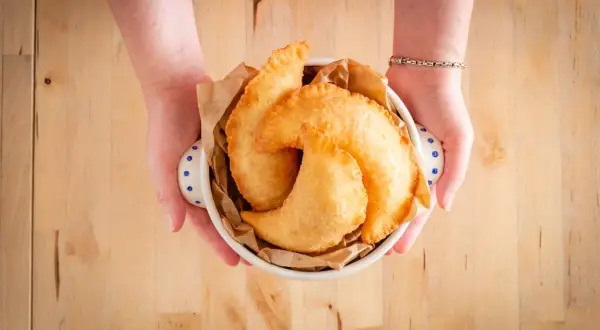 Mani che offrono un cestino di frittelle dorate, un sapore autentico di street food pugliese.