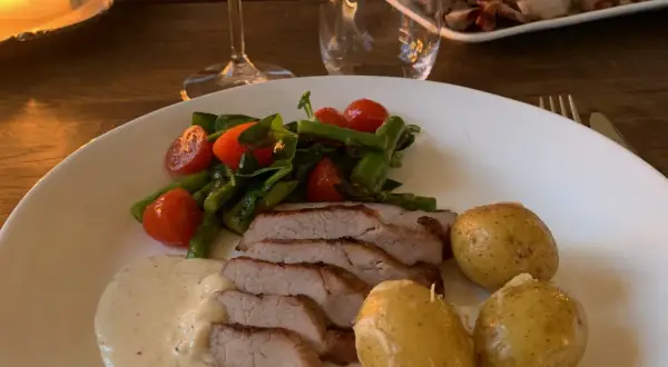 En tallrik med saftigt grillad pluma, serverad med småpotatis, sparris, körsbärstomater och en krämig sås. En härlig måltid!