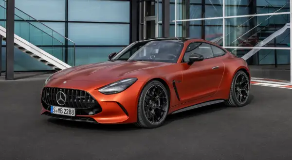 Pomarańczowy Mercedes-AMG GT 63 z czarnymi felgami stoi przed nowoczesnym budynkiem z przeszkloną fasadą i schodami.