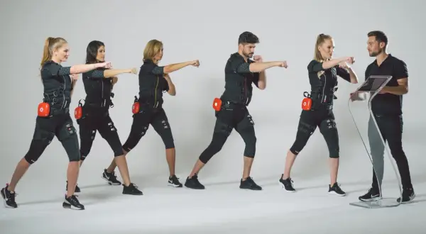 Grupa osób w strojach EMS ćwiczy pod okiem trenera. Dowiedz się, ile kosztuje trening EMS i zacznij swoją metamorfozę!