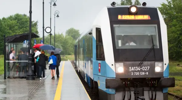 Szynobus Lublin - Zamość trasa. Pasażerowie z parasolami czekają na deszczowy dzień na peronie.