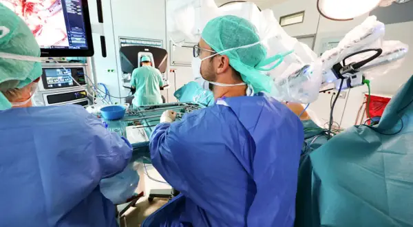 Chirurgen im OP-Saal bereiten sich auf eine onkologische Chirurgie vor, mit Fokus auf einem Monitor, der das Operationsfeld zeigt.