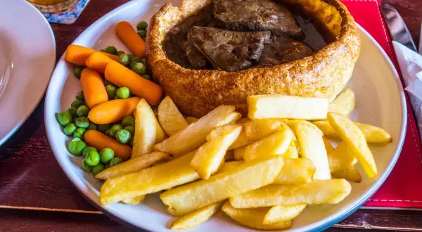 Pyszne danie kuchni brytyjskiej: pieczeń wołowa w Yorkshire puddingu, podana z frytkami, groszkiem i marchewką.