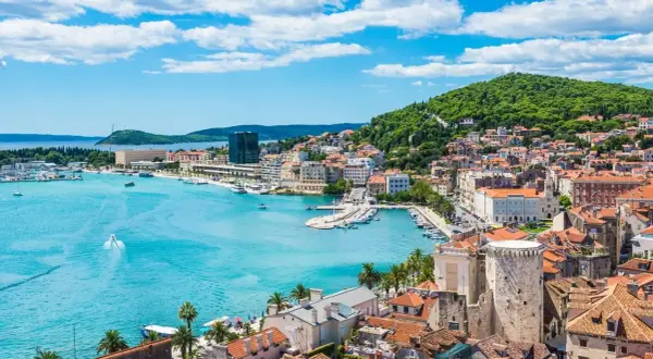 Widok na Split z turkusową wodą, łodziami i zielonym wzgórzem. Ciekawe chorwackie miasto pełne historii.