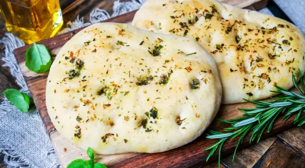Zwei knusprige pizzabrote mit knoblauch und Kräutern, garniert mit frischem Rosmarin und Basilikum.