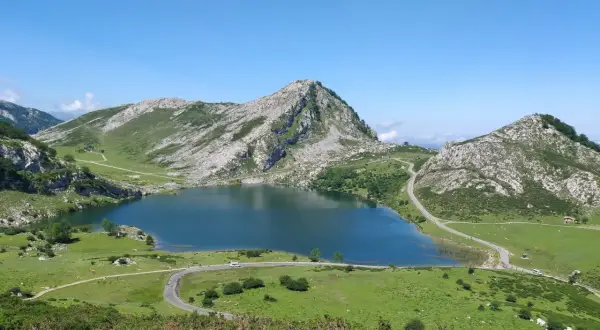 Lago Ercina en la montaña de Covadonga, rodeado de verdes prados y picos rocosos bajo un cielo azul.