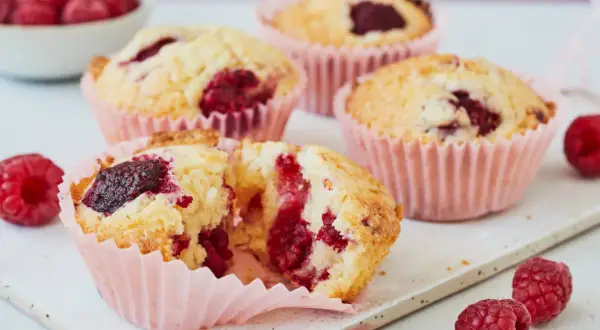 Saftige Himbeer Muffins in rosa Förmchen, mit frischen Himbeeren garniert. Ein Genuss!