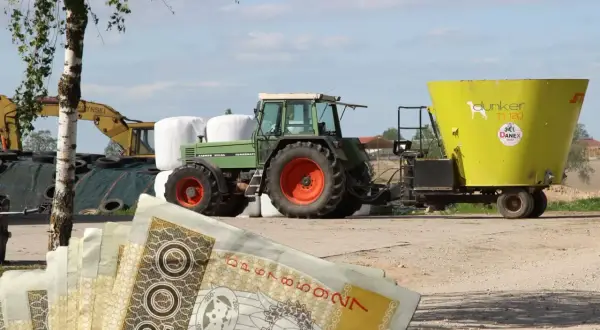 Zielony traktor z przyczepą paszową na tle pola i sterty bel. W tle koparka. Na pierwszym planie polskie banknoty 200 zł. Eudr co to? Inwestycja w rolnictwo.