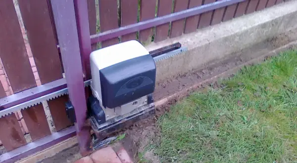 Silnik bramy przesuwnej, która po zamknięciu sama się otwiera, z widocznym zębatką i mechanizmem.