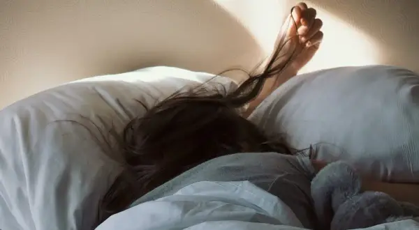 A person sleeps soundly, their hair spread across a pillow. The morning sun casts a warm glow, but the pillow rash is evident.