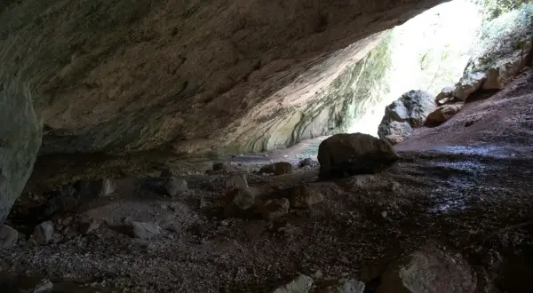 L'interno di una grotta con rocce sparse e un'apertura luminosa che rivela la valle scappuccia.