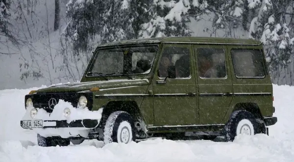 Zielony Mercedes G-klasa z napędem **awd** przebija się przez zaspy w zaśnieżonym lesie.