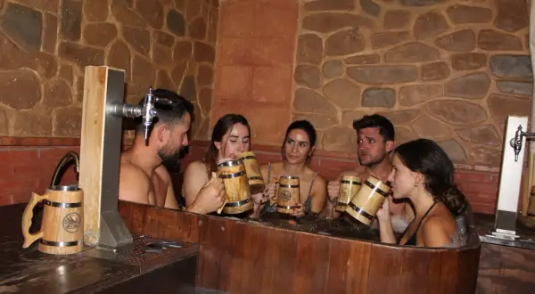 Amigos disfrutan de un relajante spa de cerveza en Valencia, brindando con jarras de madera.