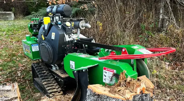 Grön stubbfräs med larvfötter redo att ta bort en stubbe i skogen.