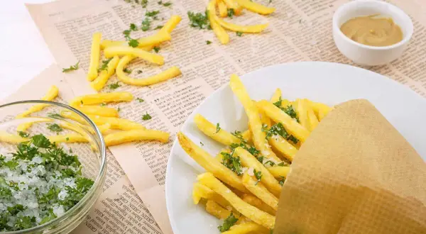 Des frites dorées, saupoudrées de persil et de sel, servies dans un cornet en papier. À côté, un bol de sel et de persil, et une petite coupelle de moutarde. Un délice qui rappelle les sardines frites.