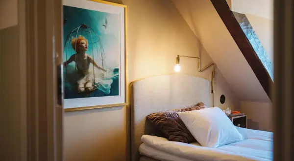 En konstnärlig tavla med en kvinna i en bur under vatten pryder väggen i ett mysigt rum på hotellet Höganäs.