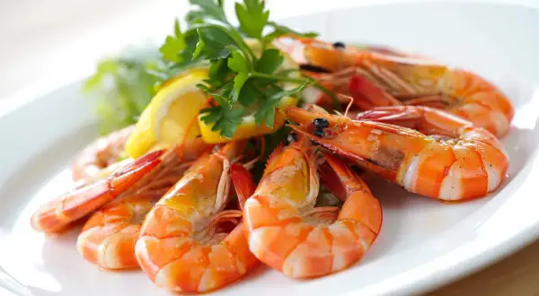 Deliciosas gambas al ajillo servidas en un plato blanco, adornadas con perejil fresco y rodajas de limón.