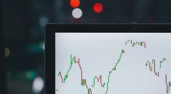 Wykres świecowy na ekranie laptopa pokazuje zmienny kurs USD JPY. W tle rozmyte światła miasta.