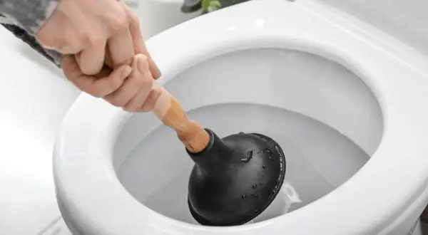 Main d'une personne utilisant une ventouse pour déboucher un WC.