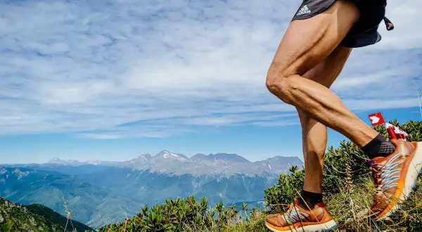 Un coureur en pleine descente trail sur un sentier de montagne, avec des sommets enneigés en arrière-plan.