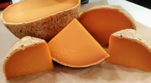 Un queso mimolette peligroso, con su corteza rústica y su vibrante interior anaranjado, se presenta en cuñas y una pieza entera, invitando a una degustación audaz.