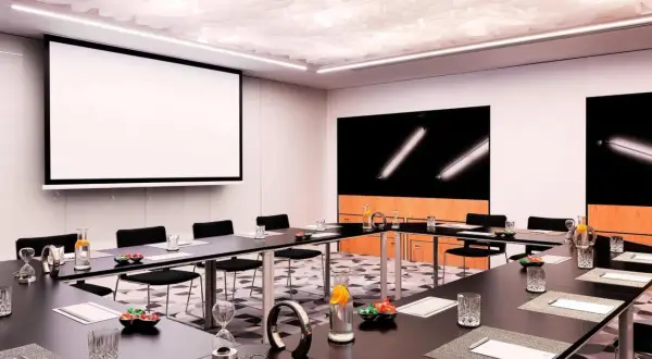 Nowoczesna sala konferencyjna w Renaissance Hotels Warszawa. Stoły, projektor, ekran i stylowe detale tworzą idealne miejsce na spotkania.
