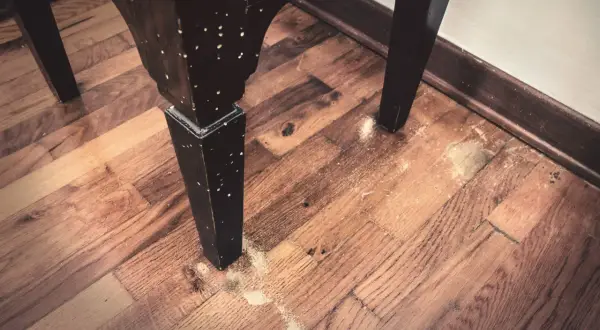 Gambe di un mobile in legno con fori e segatura sul pavimento. Potrebbe essere necessario un trattamento antitarlo fai da te.