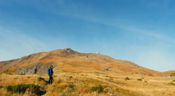Escursionista in cammino verso il monte più alto dell'Emilia Romagna, con un paesaggio dorato e un cielo azzurro.