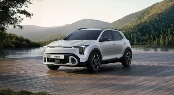 Nowy Kia Stonic 2024, biały SUV, zaparkowany na drewnianym pomoście nad jeziorem, w otoczeniu gór i lasów.