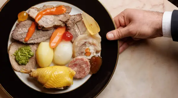 Un piatto ricco di bollito di carne, con verdure, salumi e un pollo arrosto, pronto per essere gustato.