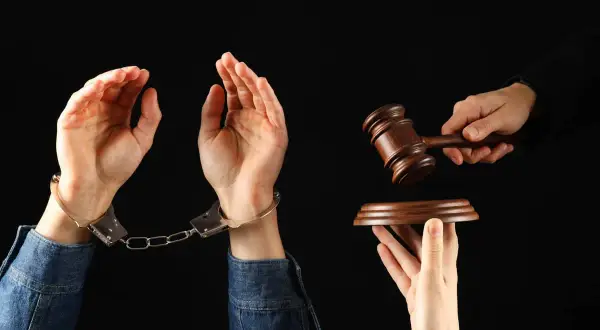 Ręce w kajdankach, młotek sędziowski i deska. Symbol naruszenia dóbr osobistych i sprawiedliwości.