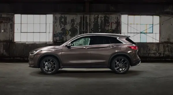 Brązowy Infiniti QX50 w profilu, zaparkowany w opuszczonym magazynie z graffiti na ścianach i dużymi oknami.