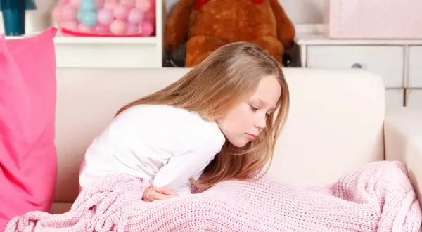 Dziewczynka z bólem brzucha, przykryta różowym kocem. Wygląda na to, że cierpi na zatrucie pokarmowe u dziecka.